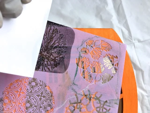 step 5 - Using an old credit card, drag the paint across the silkscreen. Immediately immerse the silkscreen and credit card in a container of water to prevent the paint from drying permanently on them. Blot them dry with a towel before using them again.