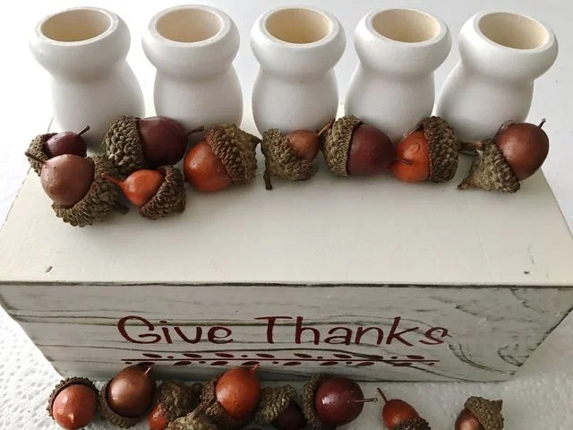 step 8 - Alternating the acorn colors and sizes, hot glue a row onto the bin in front of the candle cups. Continue filling the space then begin stacking and gluing until you've used up all the acorns.