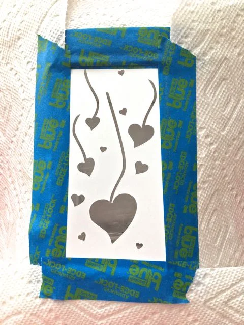 step 2 - Turn the stencil over and apply adhesive. Align the center of the card stock with the center of the glass container. Protect the rest of the glass from overspray by covering it with paper towels.