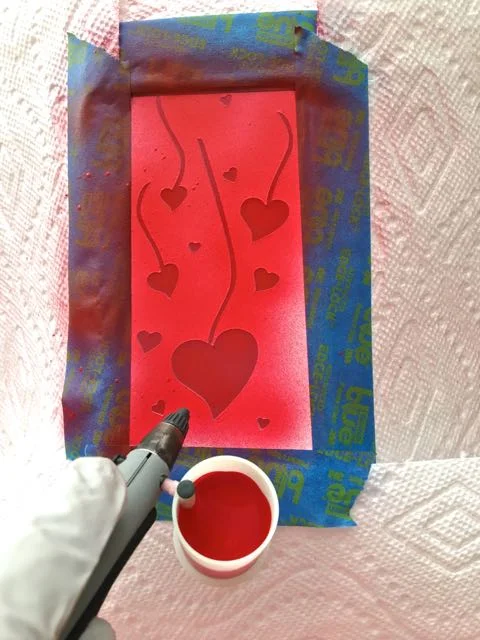 step 3 - Fill a paint cup with red paint. Airbrush the open areas of the stencil. Use several thin applications for coverage. A heavy coat may peel off when the stencil is removed.