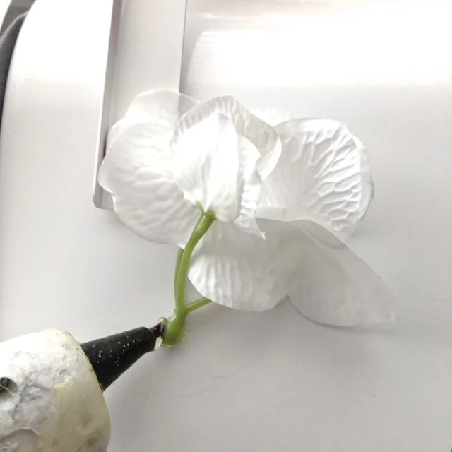 step 10 - Cut long stems off the floral picks and hot glue the greens to the mailbox. Start at the hinge of the flag, being sure it can still operate once the flowers are glued in place. Glue additional flowers up the edge of the mailbox opening. 