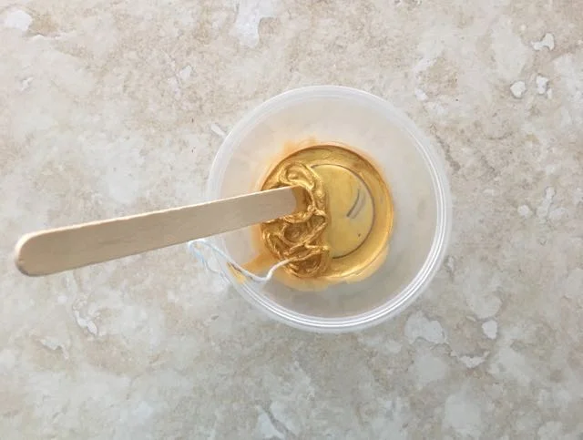 step 2 - Dip about 24” of floss into a plastic cup containing gold paint and a craft stick. Tie a knot in the end of the floss for ease of handling in the next step.