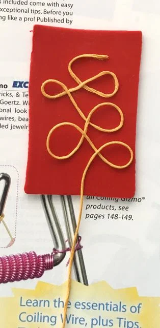 step 7 - Straighten the floss tail in the center of the clay toward the bottom edge. Allow the knot to hang outside the catalog.