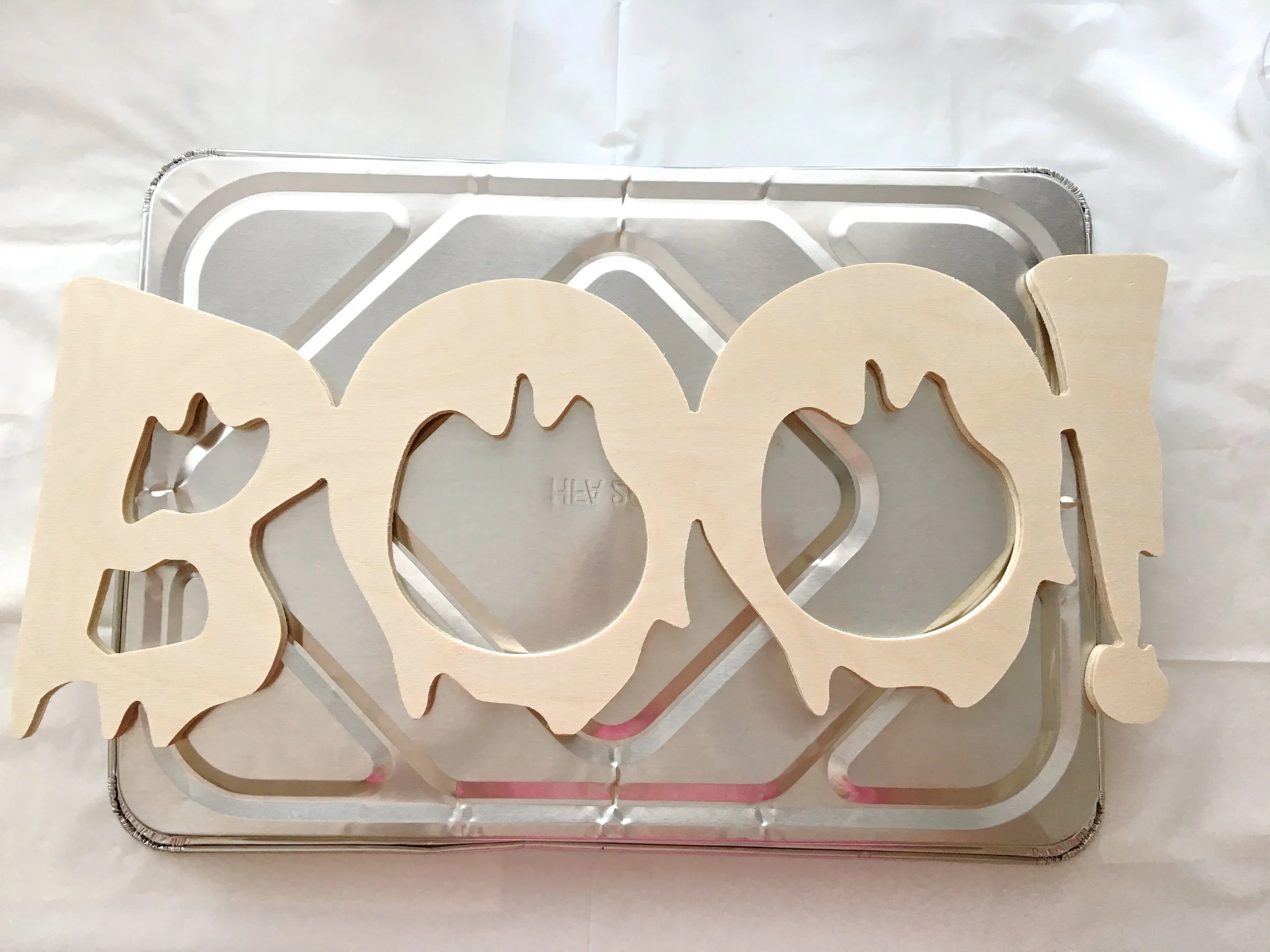 step 1 - Remove tags and stickers from the wood plaque. Set it on a disposable foil pan that is inverted to raise the plaque off the work surface. The pan will allow you to easily get underneath to tilt the wood and distribute the paint.