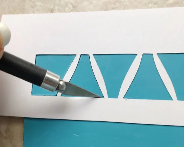 step 7 - Print out the individual bead templates and cut them out with a craft knife. You will need six center bead stencils and two end bead stencils. (If you have a stencil cutting machine like me, you can duplicate my bead templates to create one complete stencil with all the beads aligned in a row.) Place the stencil on the plain turquoise strip and cut out the shapes with a craft knife.