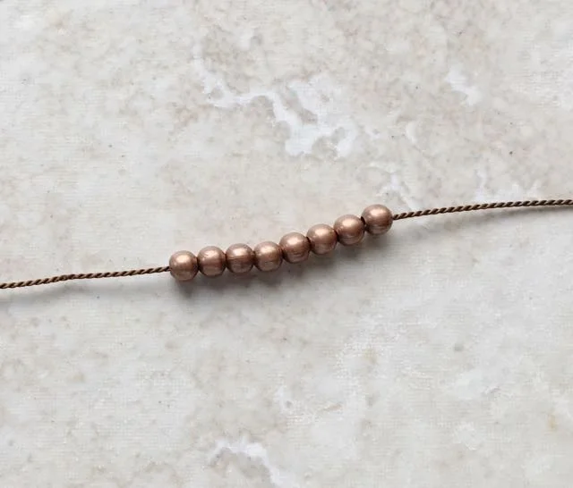 step 11 - Slip eight beads onto the needle and move them to the end of the cord. Cut the cord to measure 12”. Set it aside and create a second beaded cord measuring 12”.