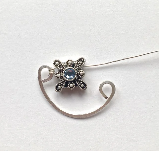step 10 - Slip the other end of the wire through the slider bead. Wrap the wire around the second curl three times. Trim and smooth the tail wires. Create three of these shapes with slider beads centered between the flattened curls.