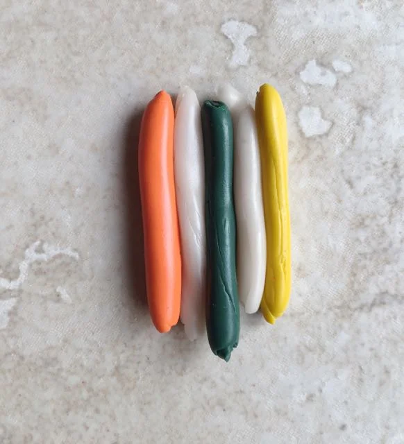 step 5 - Roll out each piece with the palm of your hand on the work surface. Place them side by side with the translucent in between the colors. Grasp them together.