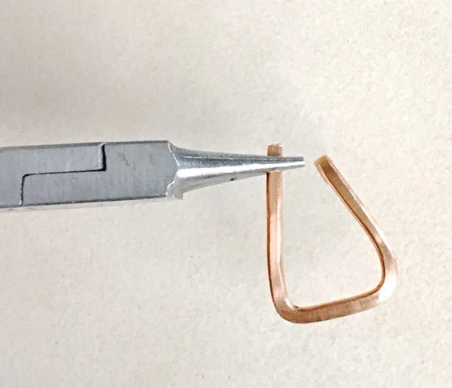 step 4 - Position round nose pliers at each cut wire end. Create equal curls to the back of the pendant. The sharp edge of each curl should be flush against the back of the flattened wire with enough of a loop for threading the cord. With a Sharpie, place marks .50” down from the curls on the front side of the frame.