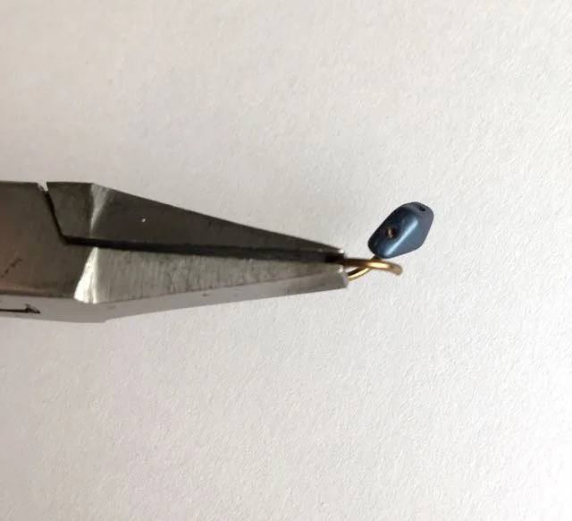 step 3 - Use pliers to open the ring a bit more, enough to insert into a hole in the duo bead. Push the wire into the bead hole until you see the tip of it. (Because the wire is curved, the bead will not slide completely onto the wire.) Using pliers, close the ring so the two cut ends meet.