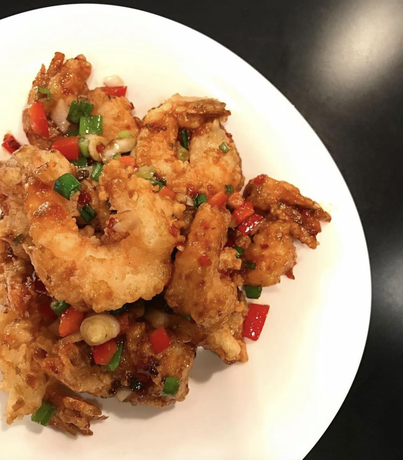 Close-up of battered shrimp garnished with chopped green onions and red peppers on a white plate.