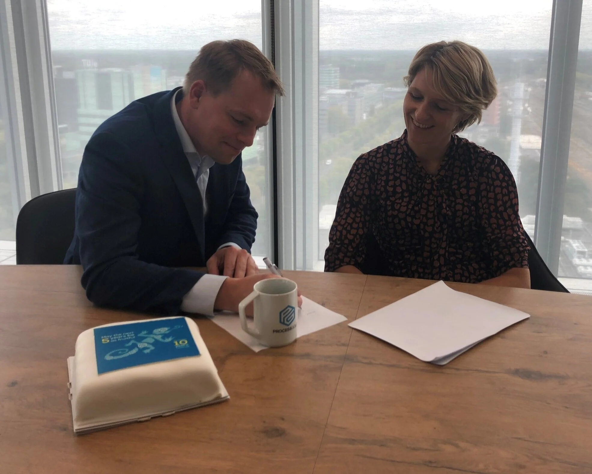 Christiaan Esmeijer van Magnaview en Maaike Goemaat van Topicus tekenen op grote hoogte het contract dat de hernieuwde samenwerking bevestigt. Daarna was er tijd voor taart.