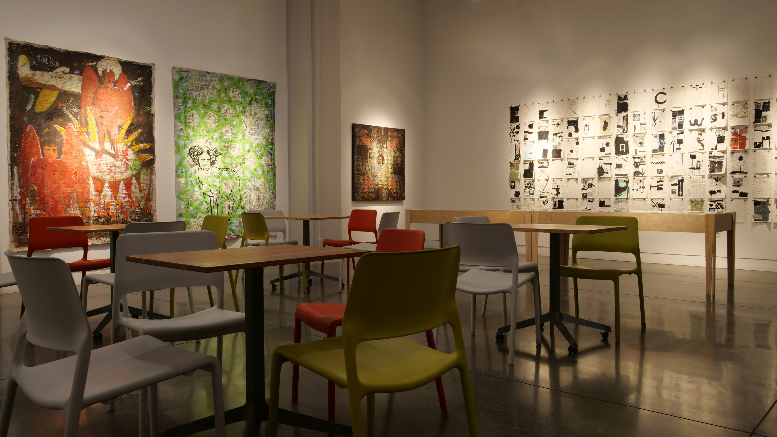 Gallery view of a wall of redacted magazine and news print behind a scattering of tables and chairs.