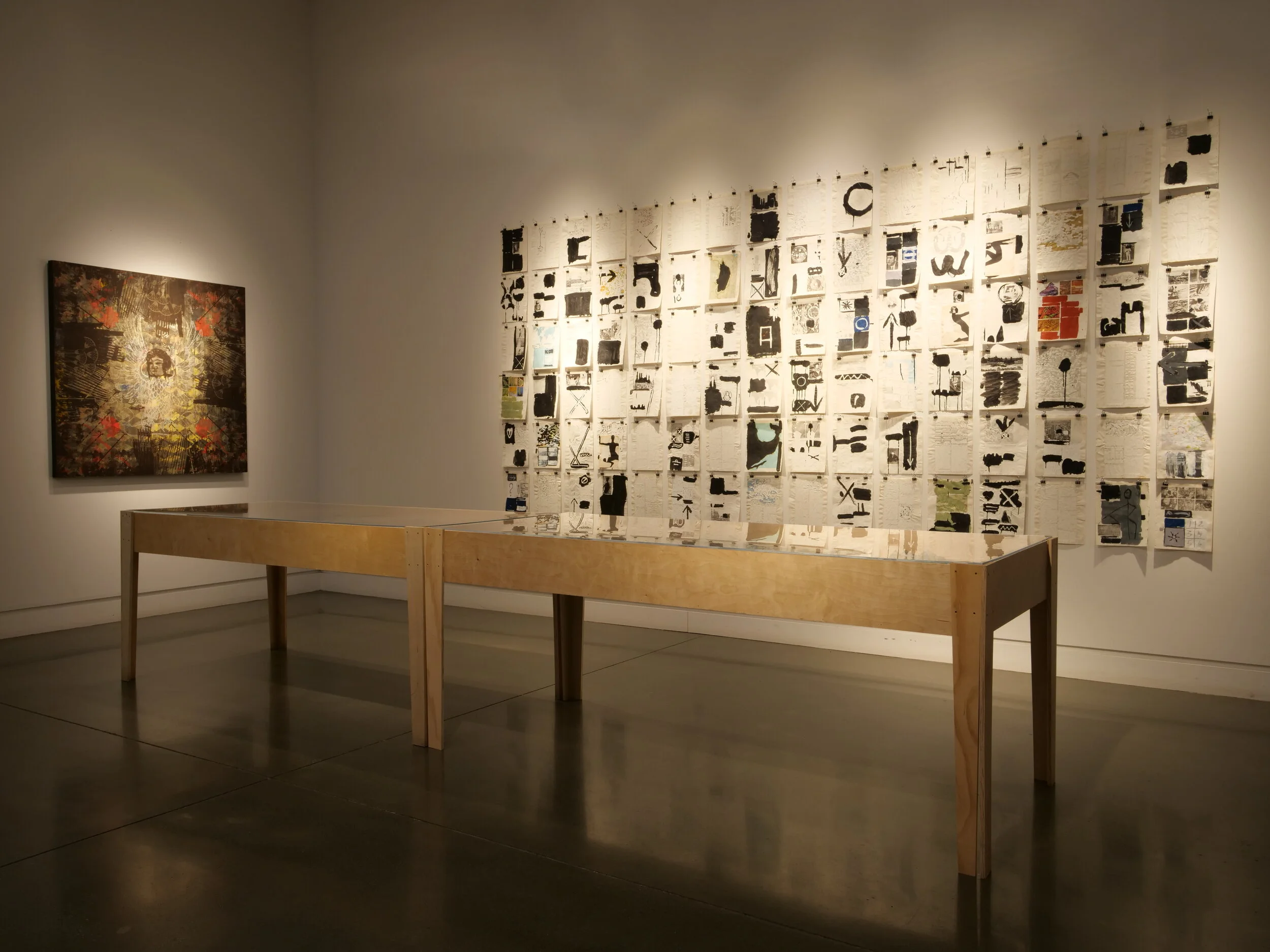 Wall collaged with redacted magazine and news print with a display table in front of it.