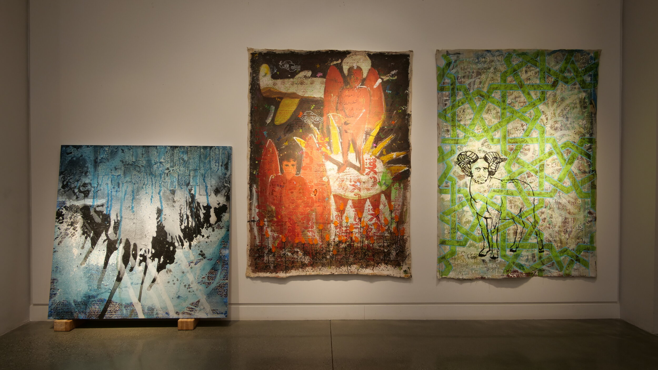 Three large-scale paintings in  a row: The left leans against the wall atop two blocks of wood.