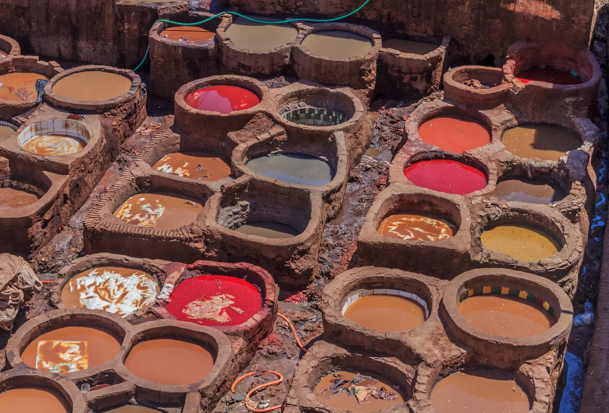 Various colorful dye pots used in traditional textiles dyeing process arranged outdoors in a haphazard manner.