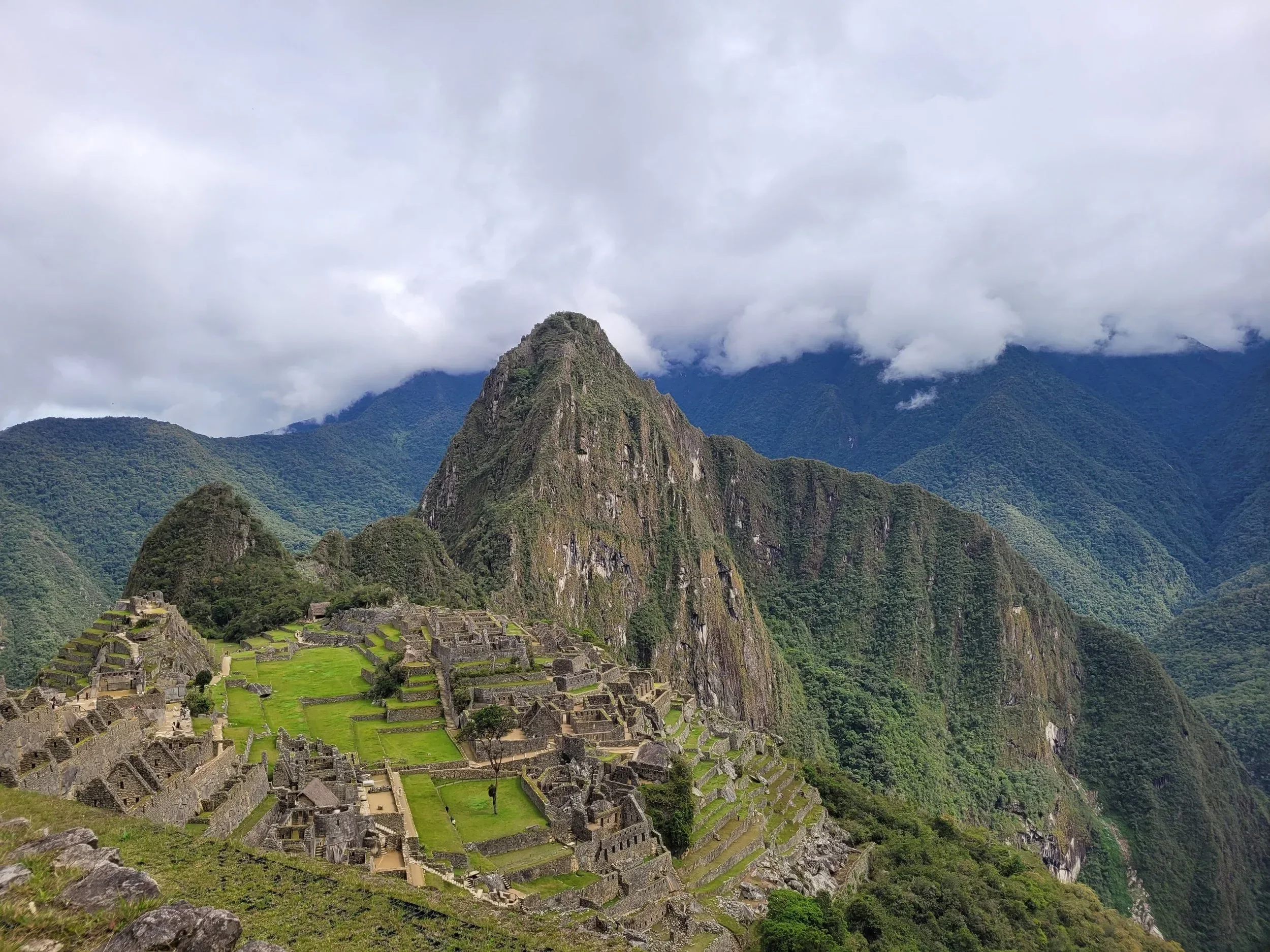 Ancient Incan city Machu Picchu surrounded by green mountains and cloudy sky.