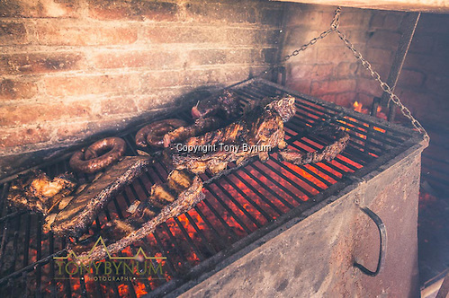 Ribs, sausage, and steaks cooking over an open pit La Pampa, Argentina ©tonybynum.com. The fire is built in the box next to the grill. As the coals become ready, they are shoveled underneath the grill.