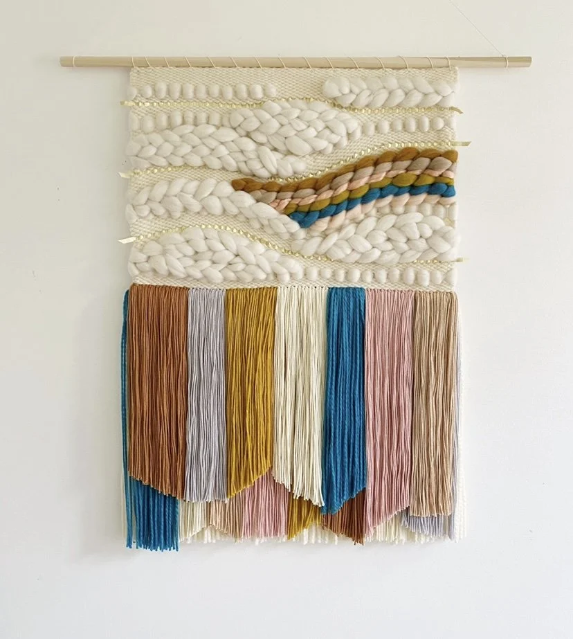 Bright Tasseled Weaving by Sunwoven featuring ivory, light grey, pink, mustard, sand, bright blue, and rust wool roving. A colorful, handmade fiber art statement piece on a wooden dowel.