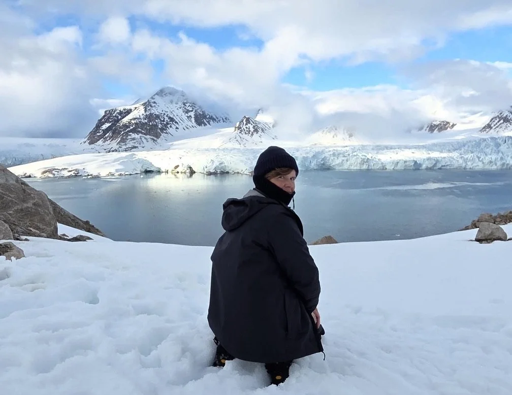 image of someone on their knees in front of a fjord and glacier