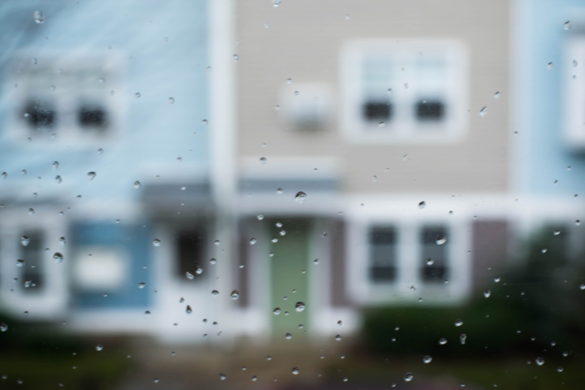 A window with raindrops. Through the window are houses with windows