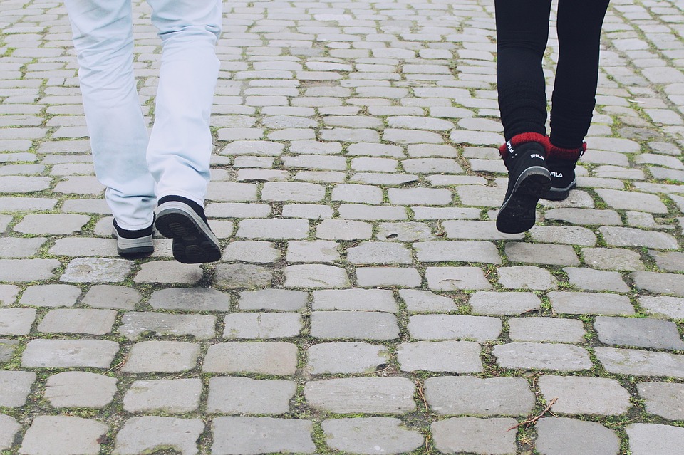 Two sets of children's feet in sneakers walk down a cobblestone street. While practicing our Alexander Technique, Acting, & Presence exercise, focus on the idea of walking. 
