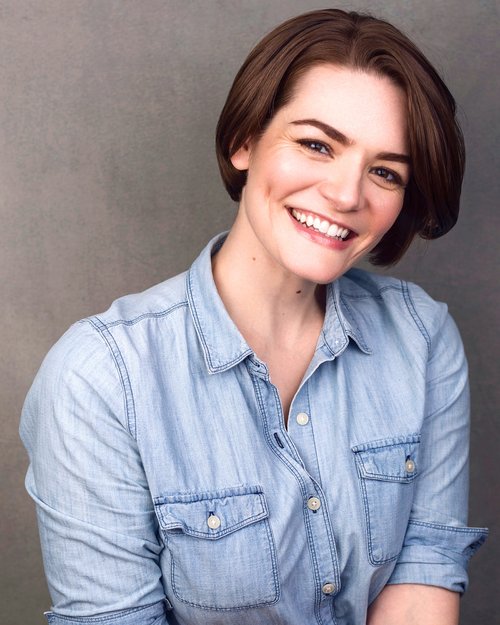 Headshot of NYC Actress: Caitlin Diana Doyle. Caitlin smiles at the camera in a light denim shirt.