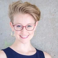 Headshot of Dana Calvey, New York City Alexander Technique teacher and Guest Instructor at AT Motion Center for Actors. Dana has short blonde hair, pink framed glasses, and smiles at the camera.
