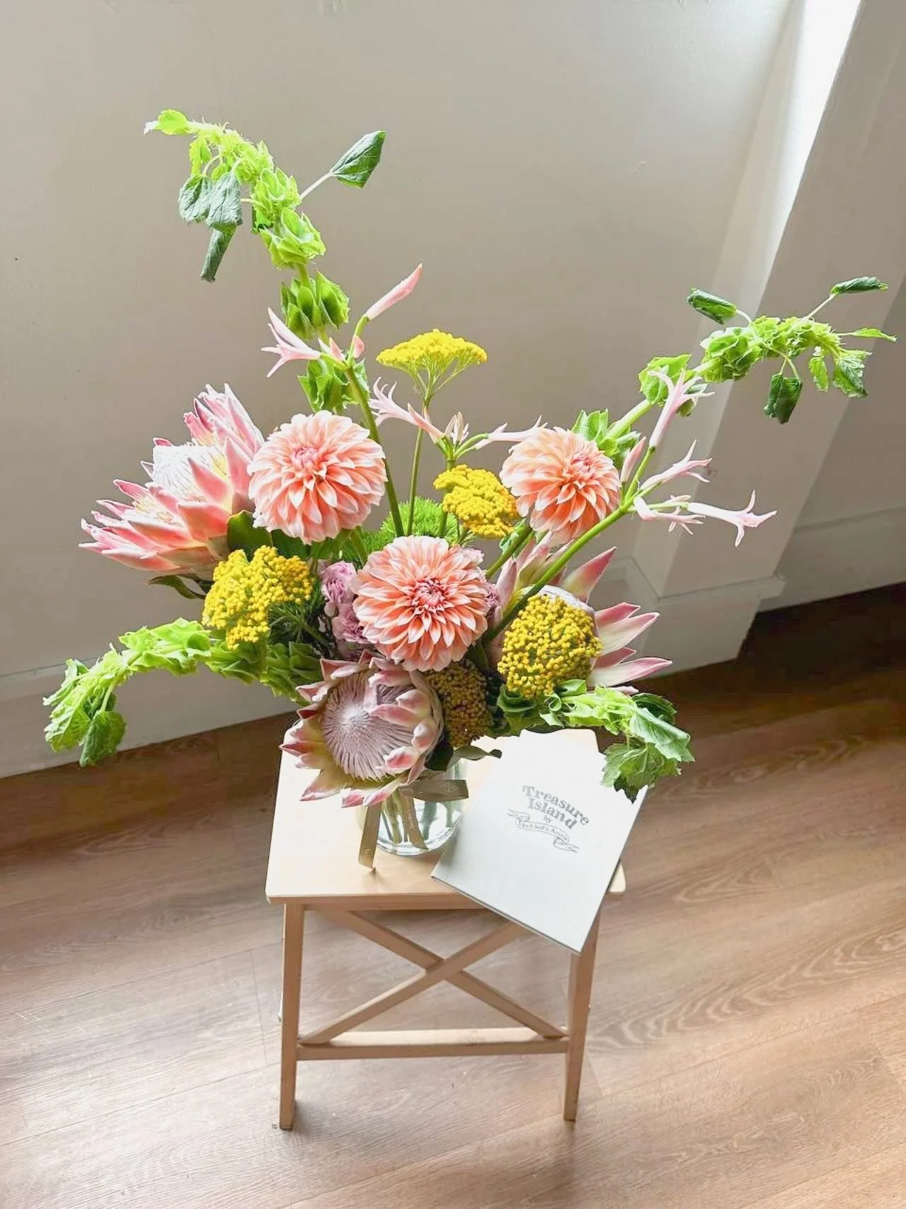 A floral treasure map, charting its own course through tropical hues&mdash;where king protea and dahlias reign over the island, mollucella painting the lush green canopies, and achillea sparkle like tiny hidden gems waiting to be found ✨