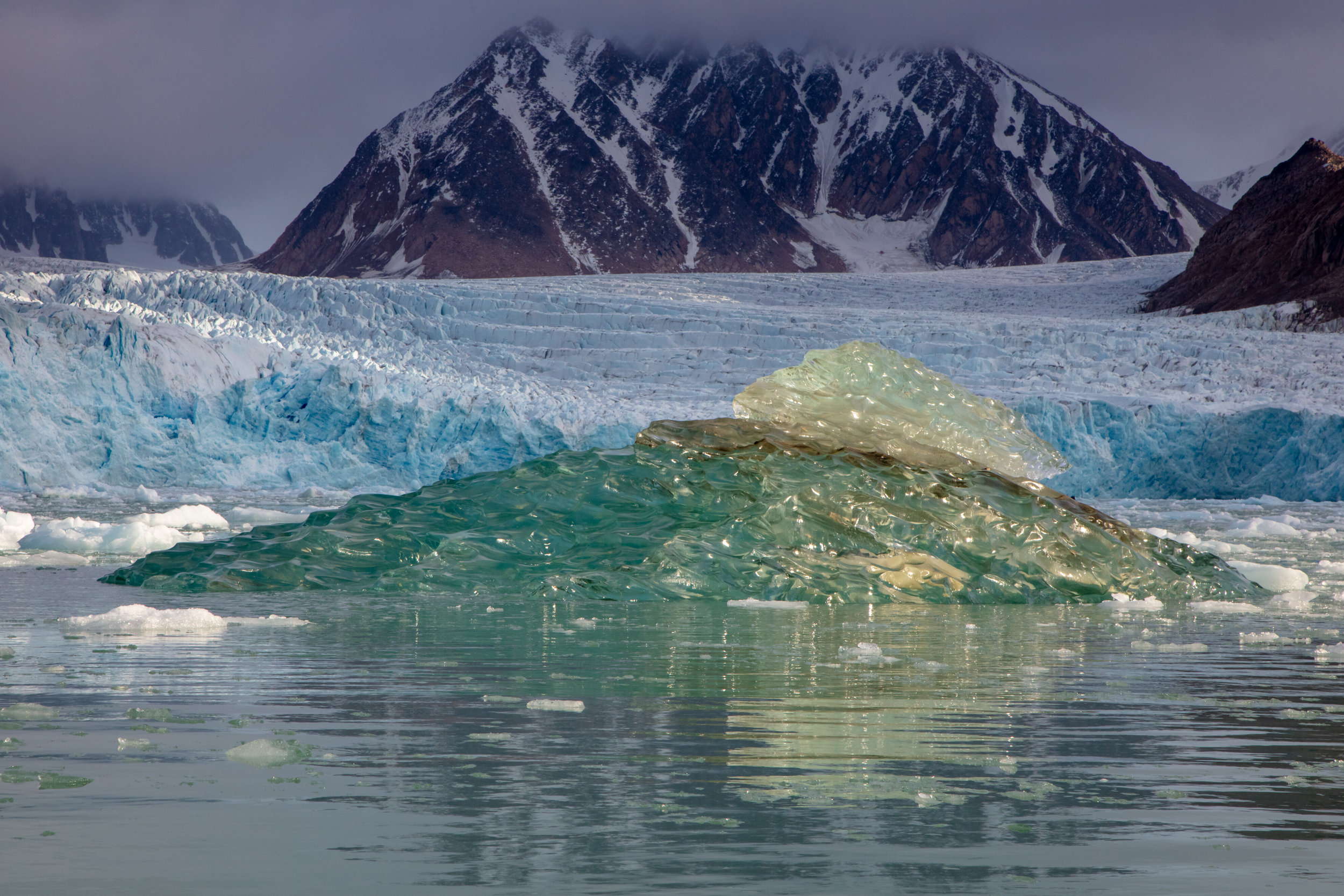 A blue iceberg drifts out to sea along the mars-like tundra of Northern Spitsbergen. Today, the archipelago of Svalbard is located just a few hundred miles from the North Pole, but this was not always the case. When these brilliant red sandstones formed 400 million years ago, the original land mass that would become Svalbard was nearly at the equator, 6000 miles south. Newly formed mountains were eroded by rivers that flowed through the once hot desert climate and the sand and mud deposited, compressing and forming stone. Though Svalbard has seen many changes along its slow journey northward, the modern geological changes are now driven by humans rather than the natural forces of nature. As the climate warms, the rapid disappearance of ice is exposing the barren rocks of Svalbard once again, possibly for the first time in thousands of years.