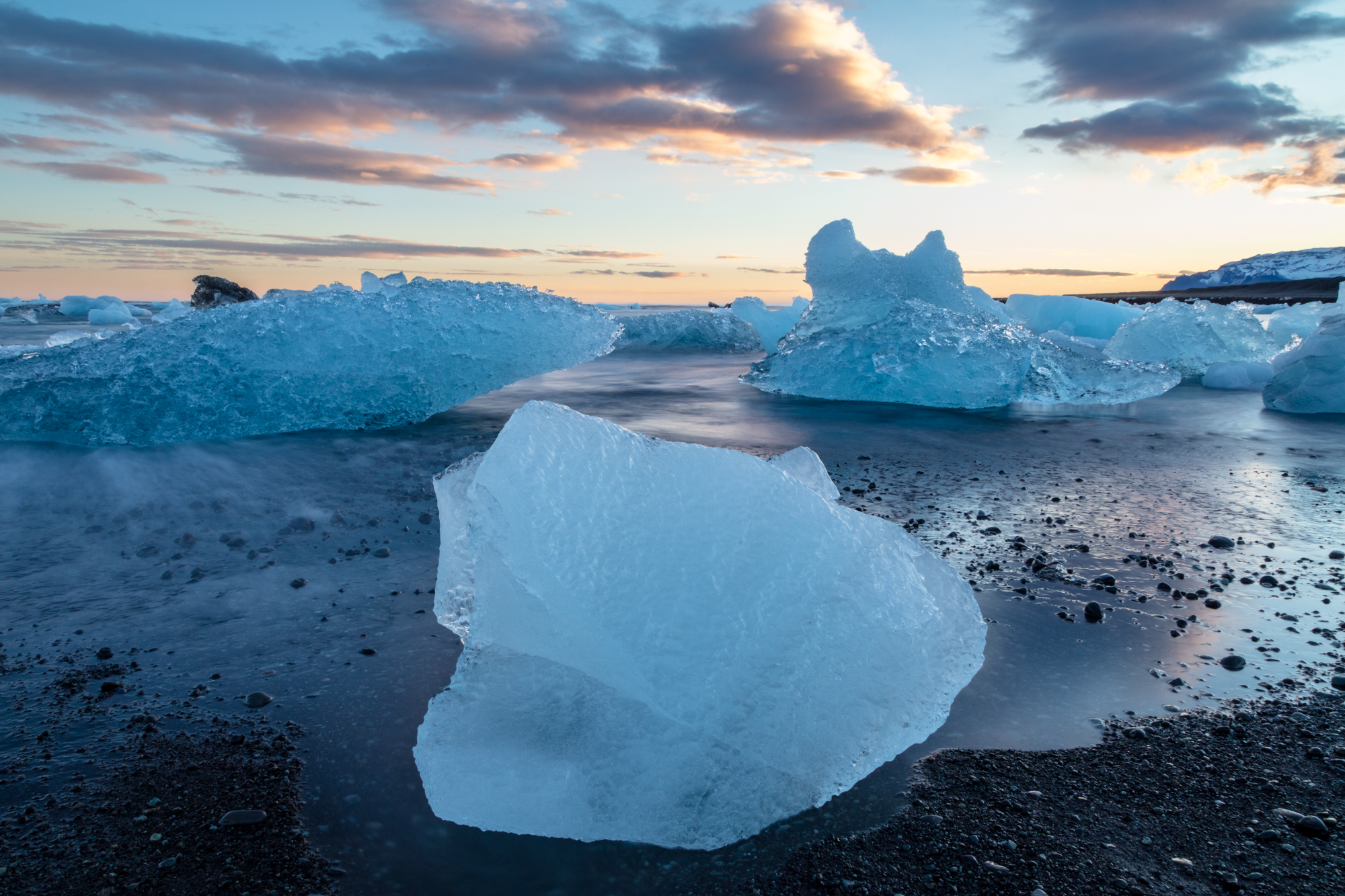 A boulder sized chunk of glacial ice sits atop a black sand beach, trapped by the shifting tides as nearby icebergs drift out to sea in the distance. I have always found icebergs to be a tragically beautiful sight as they mark the final life-cycle of glacial ice. Like snowflakes, each sculpture of ice has its own fleeting form while they drift away, rumbling and booming as they collide and collapse in the crashing waves.