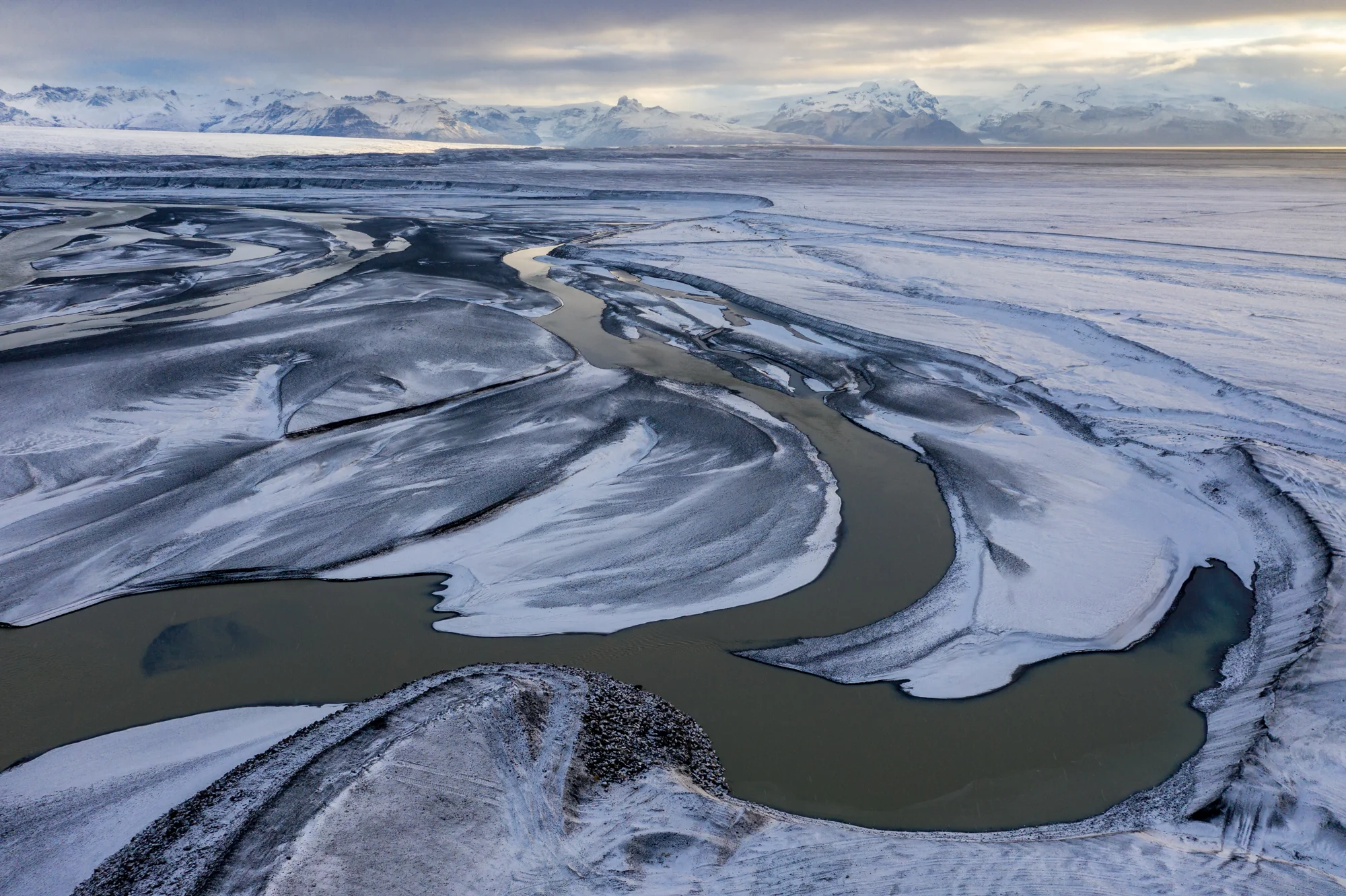 A glacial river snakes through Skeiðarársandur (a massive glacial outwash plain) as a dusting of snow is illuminated by the first soft golden light of sunrise. As the nearly 10 mile-wide Skeiðarárjökull glacier (top left) recedes back into the mountains, the sediments from the peaks that once stood in the glacier's path formed the largest sandur (glacial outwash plain) on earth, covering nearly 1300 square kilometers. This is no coincidence. The combination of active volcanic activity beneath the glacier's surface and a warming climate make the glacier susceptible rapid melting and flooding that washes through the barren landscape. Scenes like this make it easy to feel helpless to the massive scale nature's power, yet the decisions people make today influence the planet on a geologic scale.