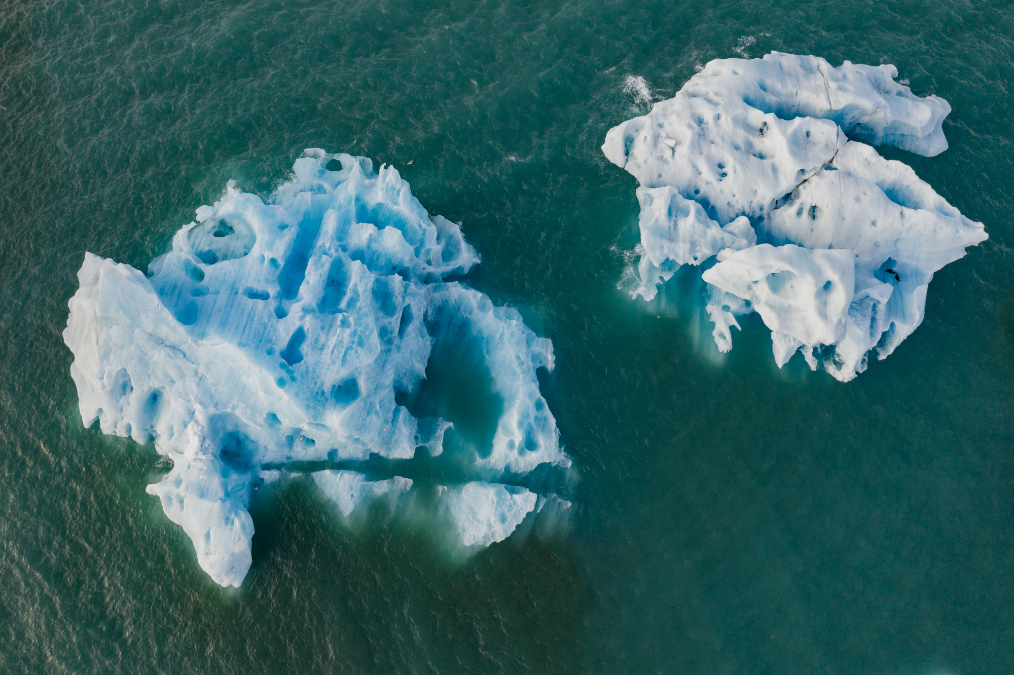 Two house-size icebergs float towards the sea in a glacial lagoon formed by the glacier Breiðamerkurjökull. Thanks to Vatnajökulsþjóðgarður National Park, who allowed me special photographic permissions, I was able to capture images of the ice from an aerial perspective. Day after day, icebergs like these break from the deceptively permanent wall of ice at the edge of the Breiðamerkurjökull, drifting into the now massive glacial-melt formed lagoon that only began to appear in the mid-20th century.