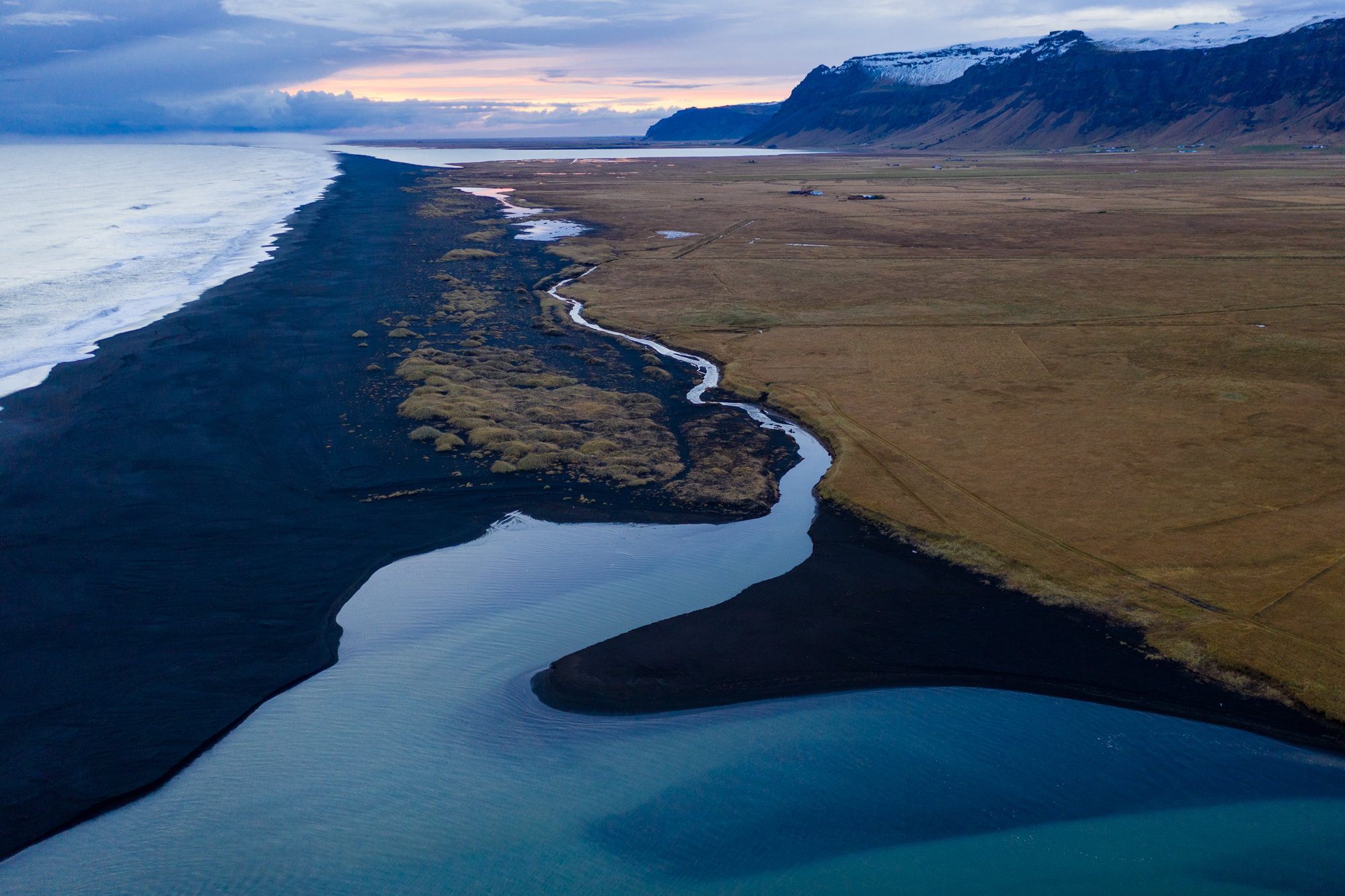 A turquoise-colored stream glows in the afternoon light as a coming storm approaches the barren coastline of southern Iceland. 