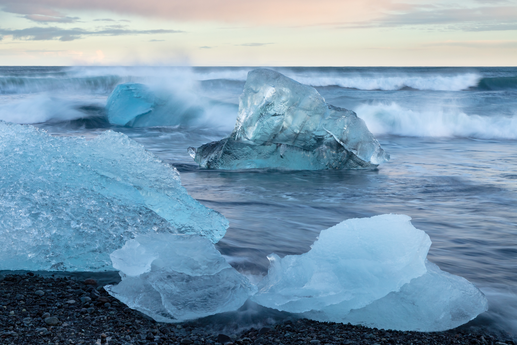 When it comes to nature photography, sometimes the most spectacular scenes come when you least expect. At sunset I discovered this strikingly clear iceberg being battered by the waves as the tide slowly gradually came up. Though I was set up for the sunset, I decided to wait a few more minutes to see how the light would change. The sunlight slowly disappeared behind the horizon and the icebergs appeared to glow under the soft cast of ambient light. As wave after wave crashed and tumbled the coast, each iceberg took on its own unique hue of blue and green, indicating part of their history in the glacier during their final moments as glacial ice.