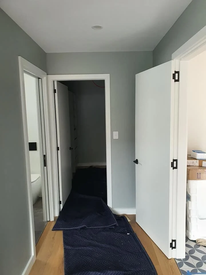 Hallway with doors, some covered with dark blue moving blankets, leading to what appears to be a closet and a partially visible bathroom.