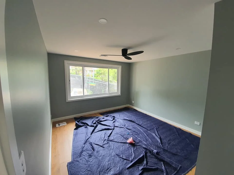 Empty room with a window, ceiling fan, and a dark blue tarp on the floor.