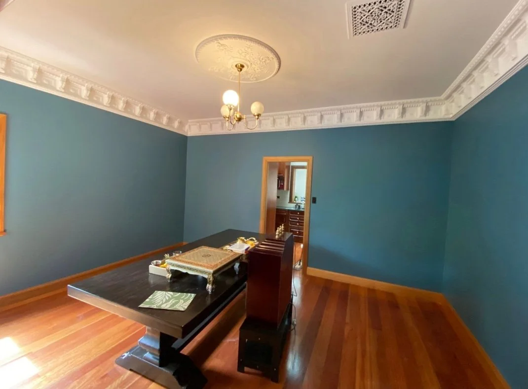 Empty dining room with blue walls, a chandelier, a black dining table, and wooden floors, with an open doorway leading to a kitchen.