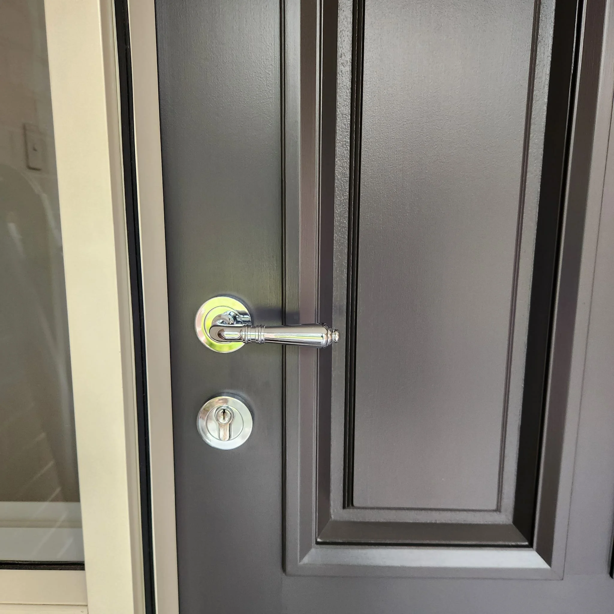 Close-up of a black door with a silver handle and lock, part of a gray wall with a beige trim.