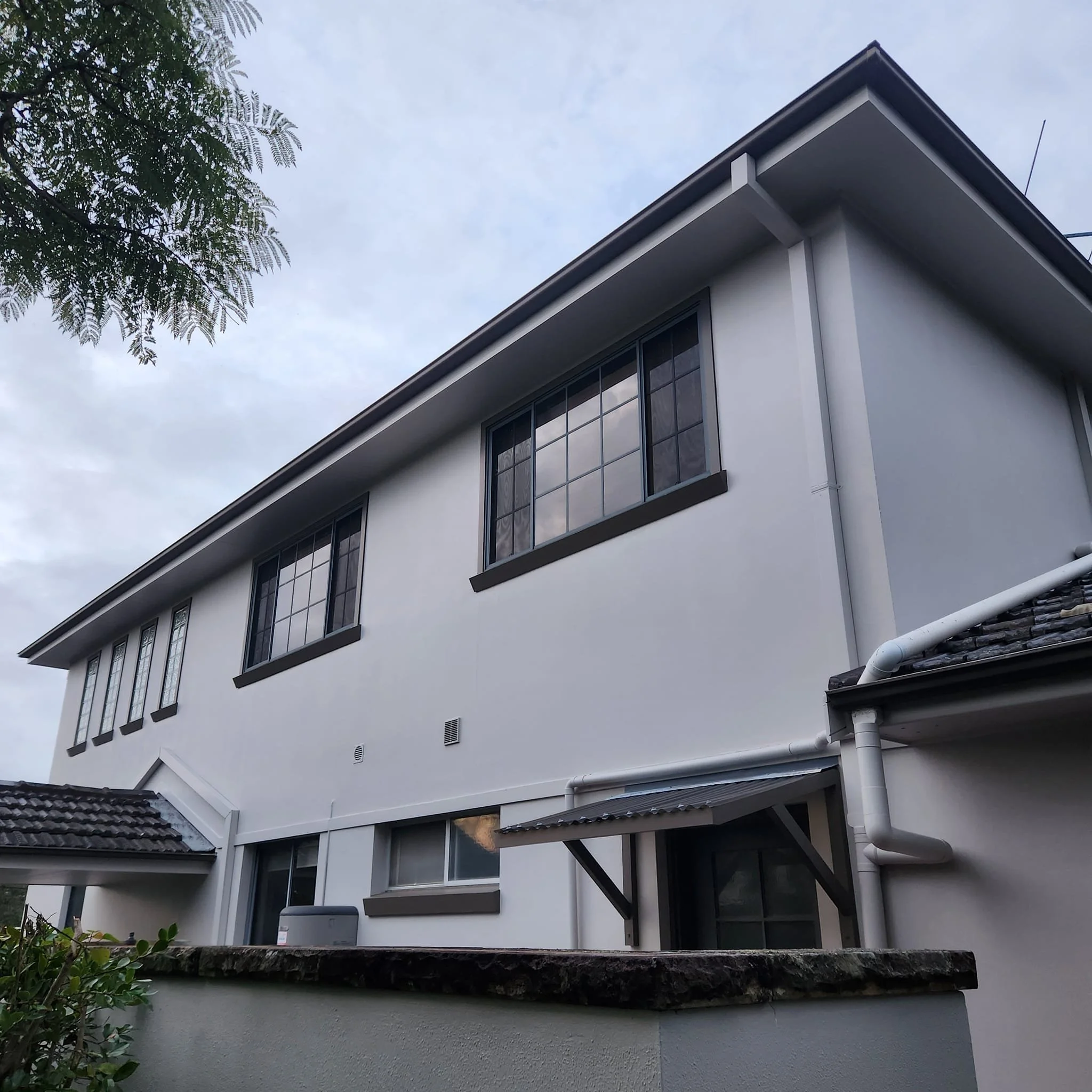 A multi-story modern house with white walls, black window frames, and a tiled roof under a cloudy sky.