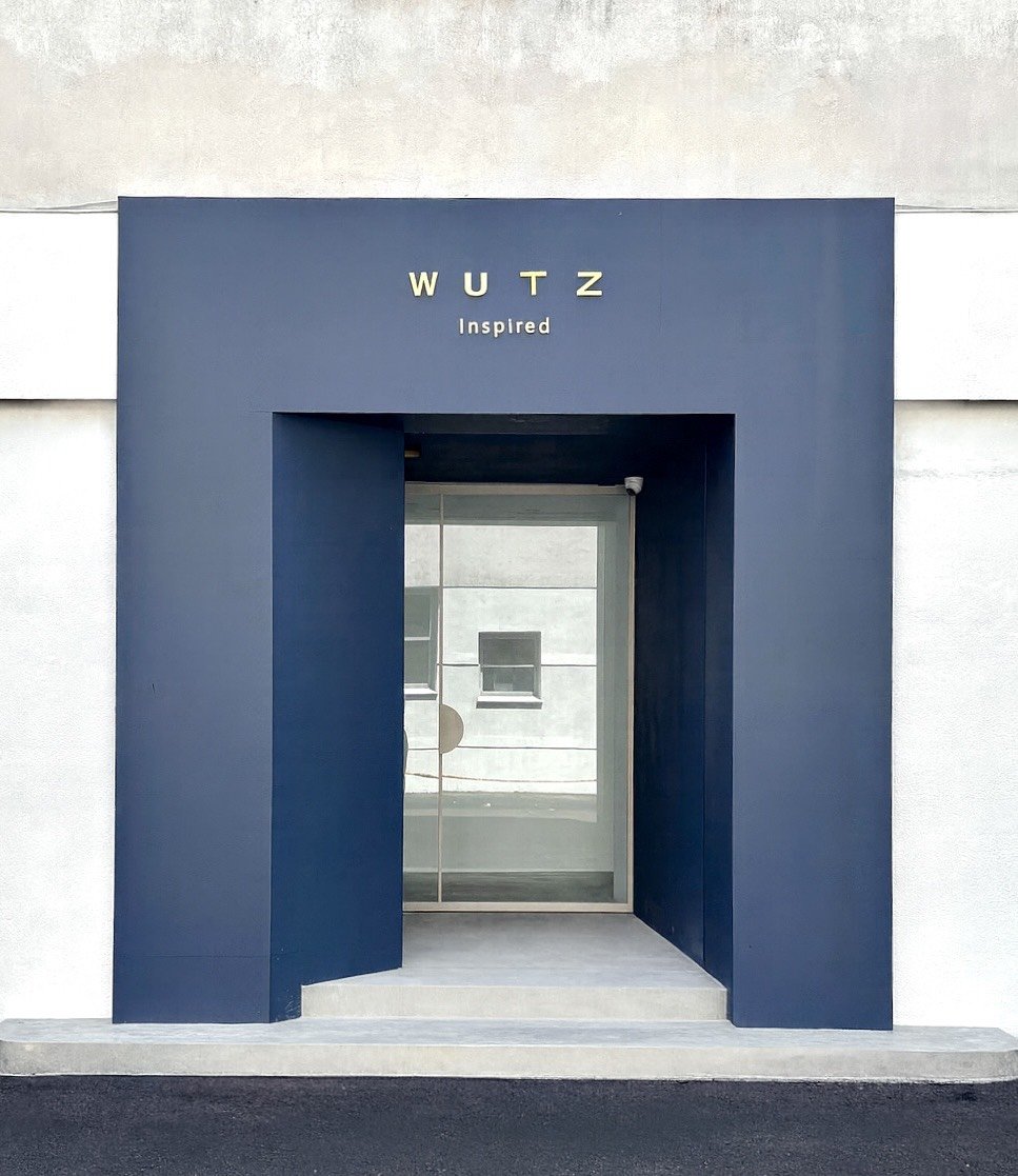 Modern building entrance with a dark blue frame and glass door, with the word 'WUTZ' and 'Inspired' written above.