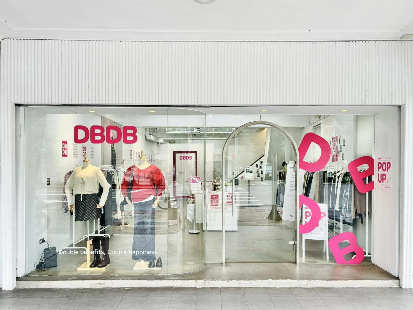 Storefront window of DDB with mannequins dressed in casual clothes, pink DDB signs, and clothing racks inside.