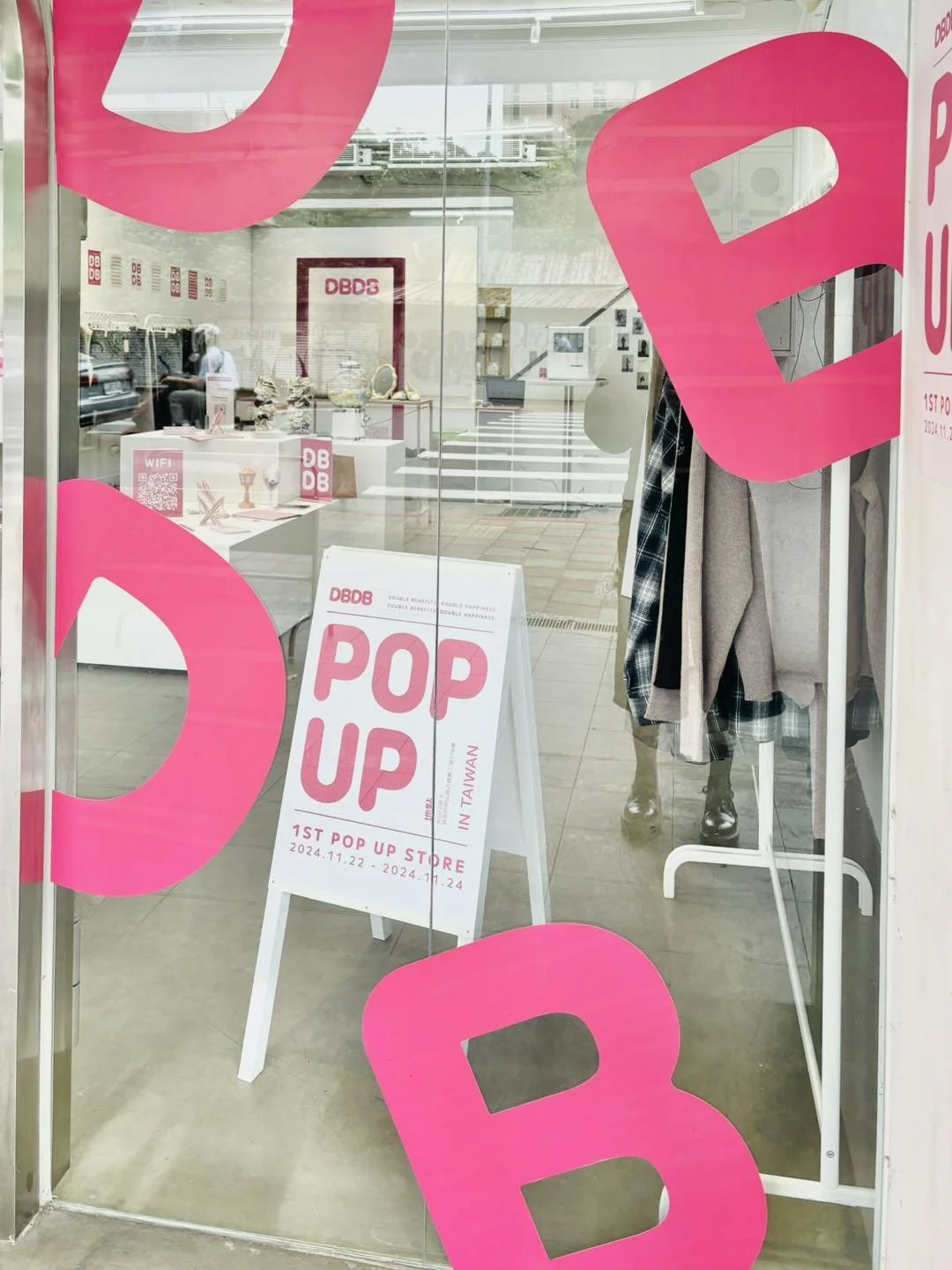Store window with pink letters spelling 'POP UP' promoting the first pop-up shop in Taiwan from November 22 to November 24, 2024, with clothing and display items visible inside.