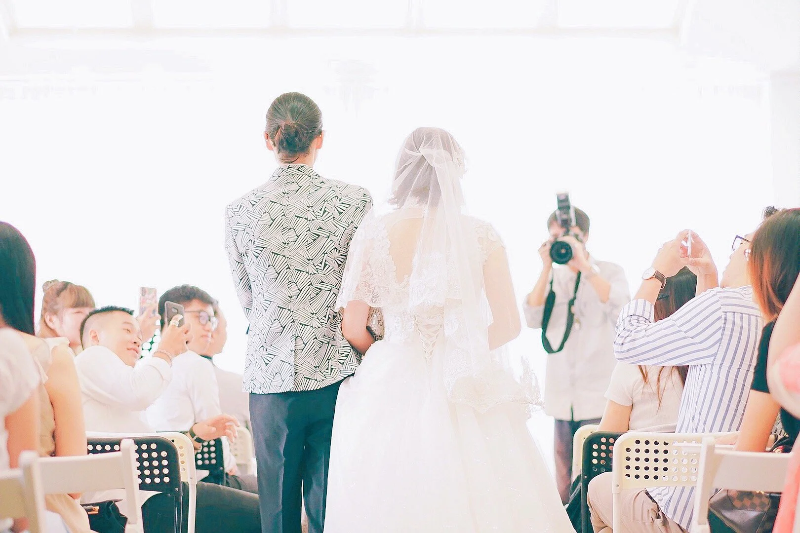 A wedding ceremony with a bride and groom standing at the altar, surrounded by guests taking photos and videos.