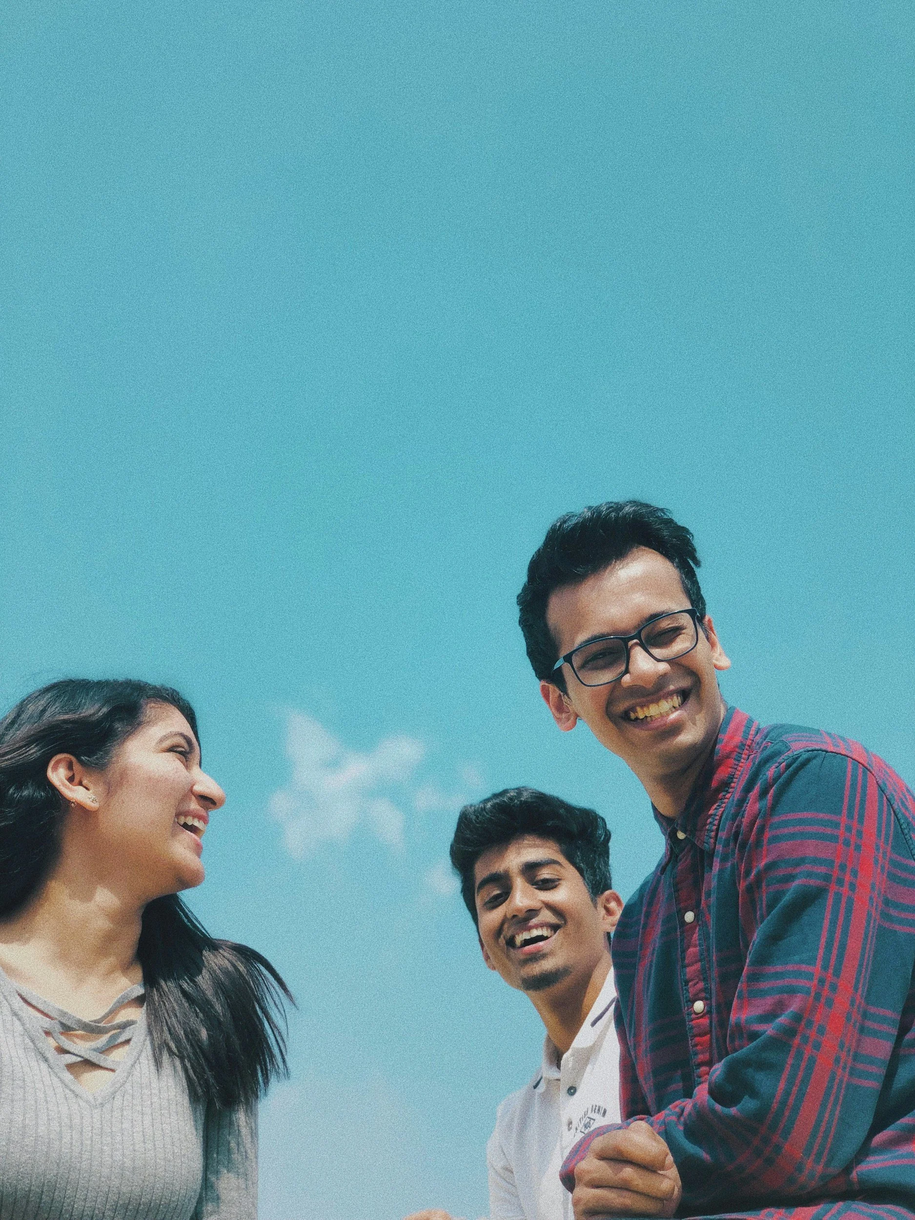 Three smiling young professionals looking up against a clear blue sky