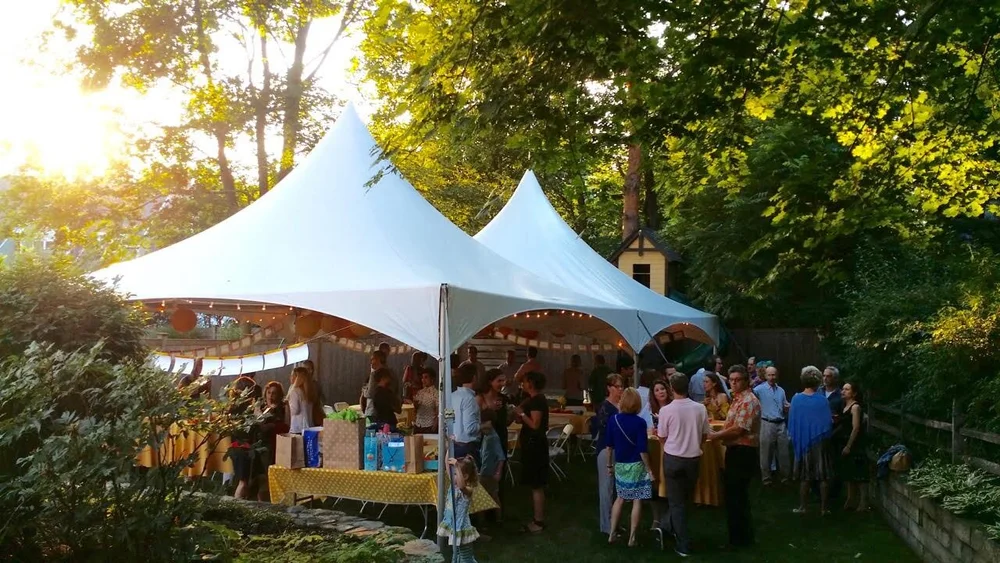 White tent lit up in a backyard with guests at dusk