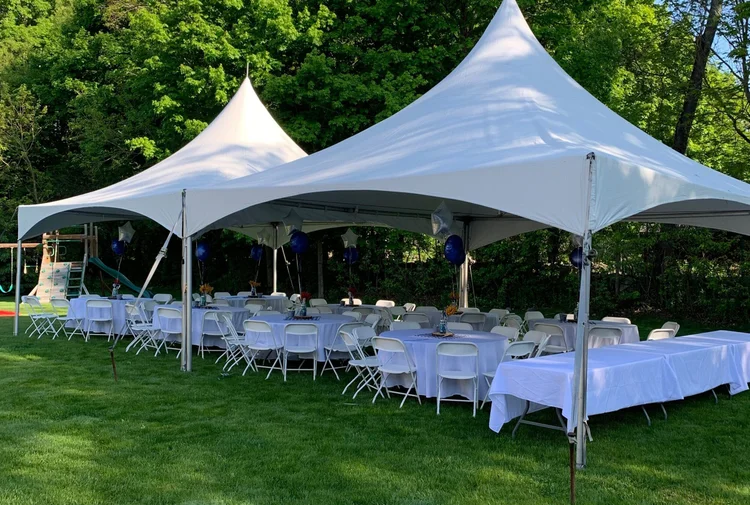 Two white high-peak tents with long rows of tables and chairs on a lawn
