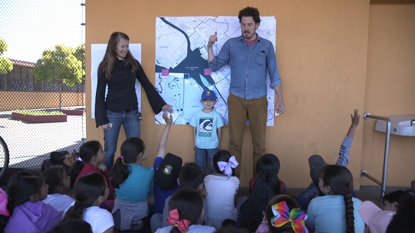 Claire and Nico (6ft) and kid (3ft) talking about SLR with a group of primarily Hispanic 6-7 year olds