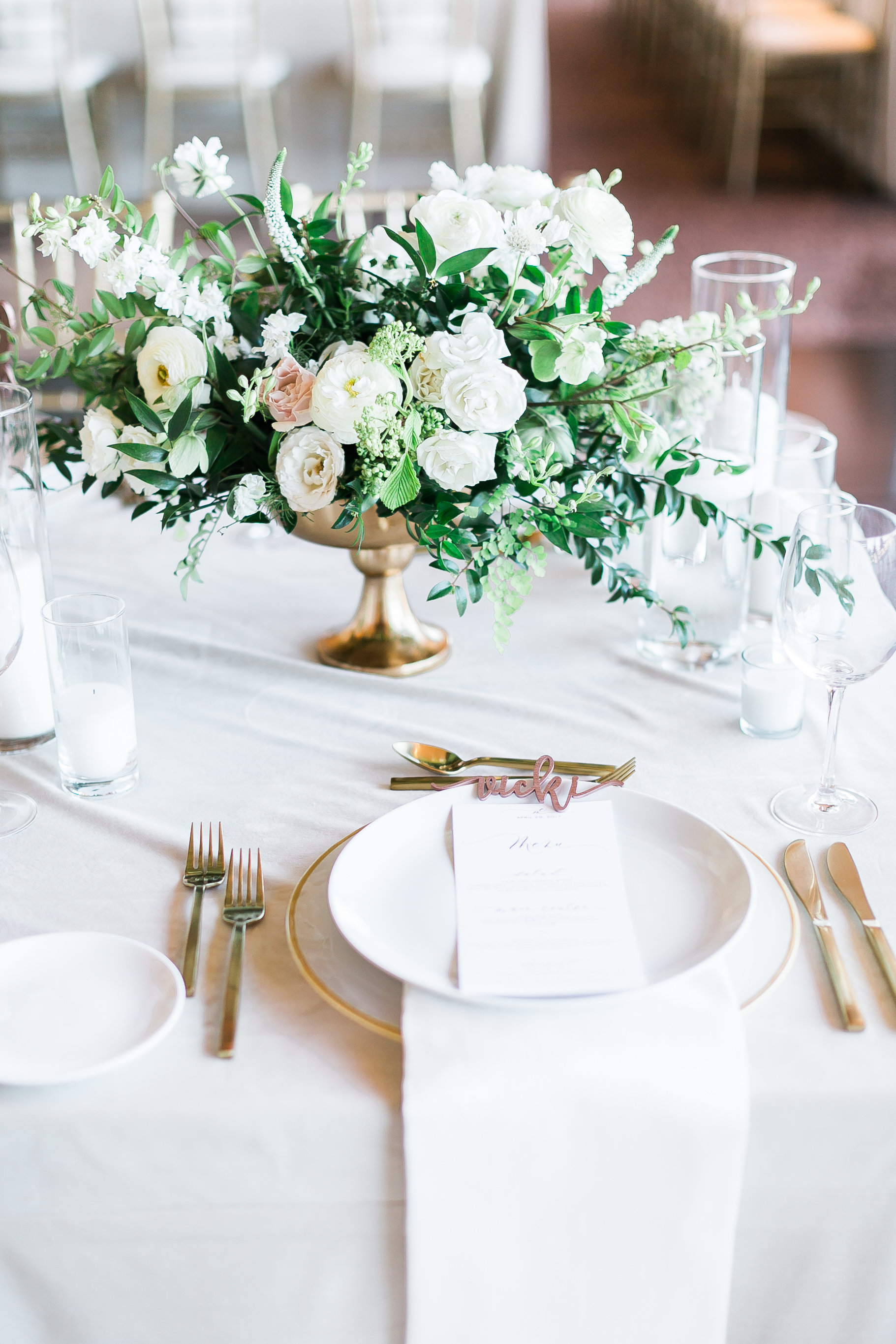Gold compote vase filled with overflowing greenery and white florals 