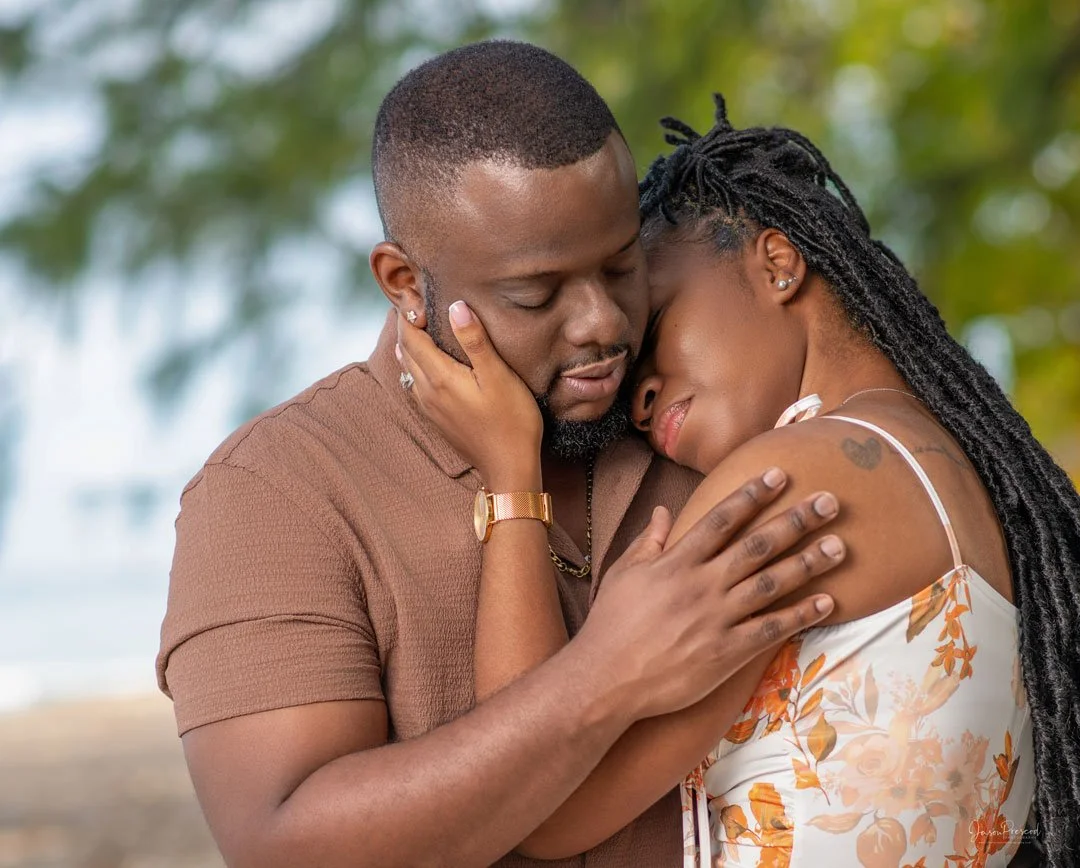 A loving couple embraces each other closely outdoors, with eyes closed, showing affection and intimacy.
